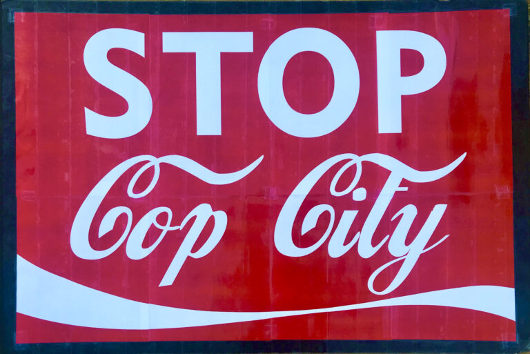 image shows a sign that reads "stop cop city" in the font and style of the Coca Cola logo
