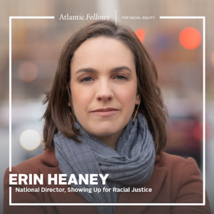 Image shows a white woman with shoulder length brown hair, looking intently into the camera. She is wearing a scarf and a brown coat. The text reads "Erin Heaney, national director, showing up for racial justice."